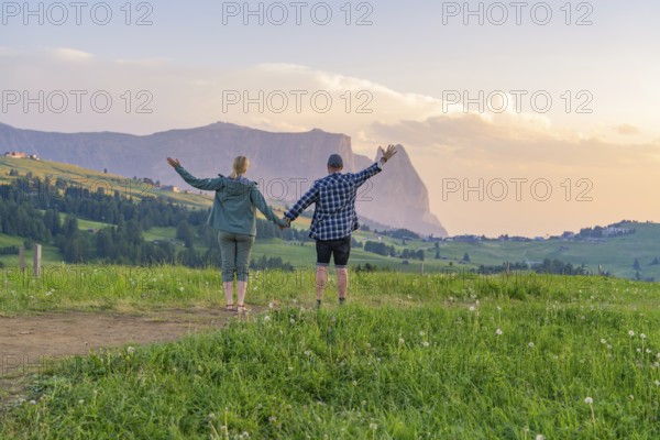A couple raises their arms in joy at the sight of the mountain landscape and the evening sky, Alpe