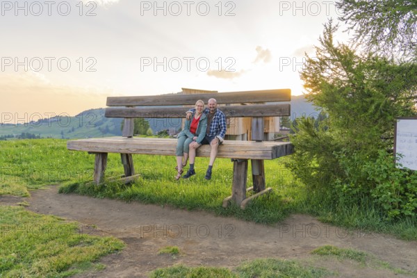 A couple sits on an oversized bench and enjoys the sunset, Alpe di Siusi, Dolomites, South Tyrol,