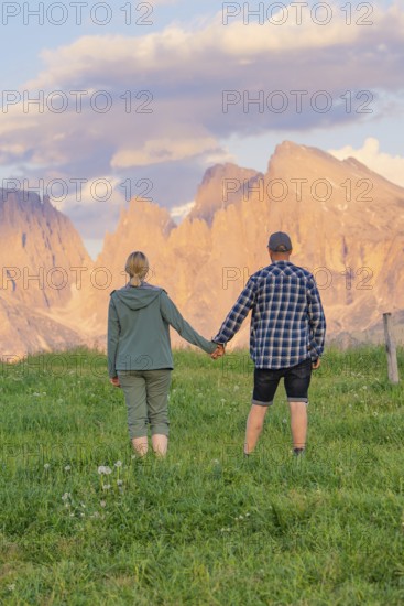A couple holding hands in a meadow against an impressive mountain backdrop, Alpe di Siusi,