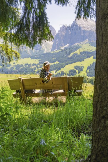 Person on a bench smiling with a peace sign in front of the mountains, Alpe di Siusi, Dolomites,