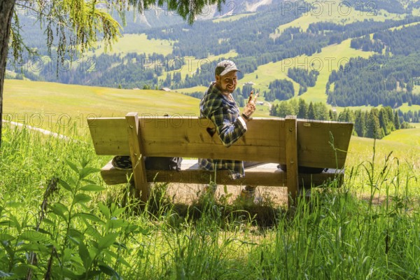 Smiling person on a bench with a peace sign in front of mountains, Alpe di Siusi, Dolomites, South