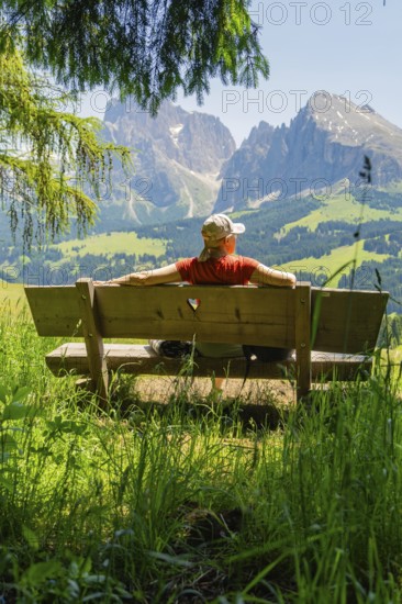 Person on a bench with a view of majestic mountains and vast landscape, Alpe di Siusi, Dolomites,