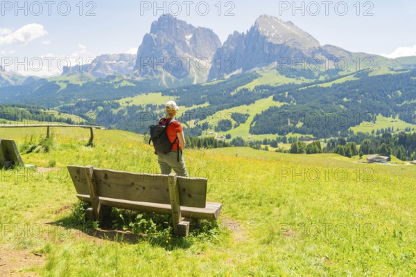 Person stands next to a bench and enjoys the view of the mountains, Alpe di Siusi, Dolomites, South