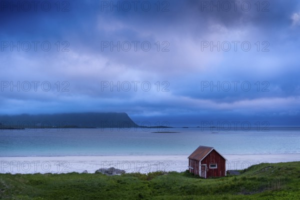 A red wooden hut on the sandy beach of Ramberg (Rambergstranda), sea and mountains. At night at the