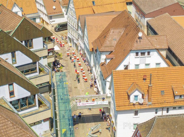 Aerial view of people moving through narrow streets of a half-timbered town under a bright sun, 950
