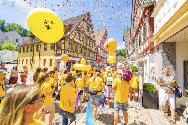 People in yellow T-shirts celebrate in a narrow street with half-timbered houses under colourful