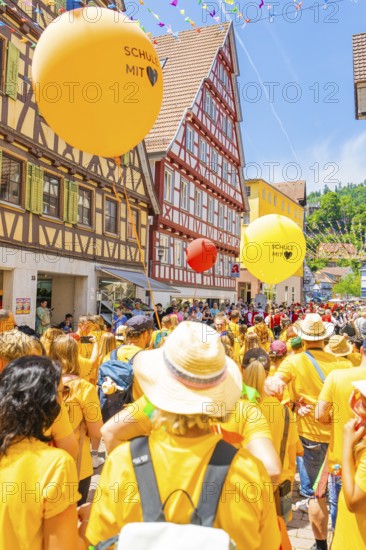 Crowd of people with orange and yellow balloons at a town festival in a half-timbered house