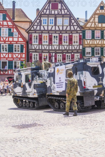 Military vehicles on a square in front of half-timbered houses, soldiers in camouflage, flowers in