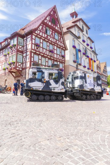 Military vehicles in front of a historic half-timbered building in a sunny old town, 950 years of