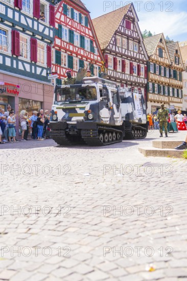 Military vehicles in a parade through a cobbled street with half-timbered houses, 950 years of