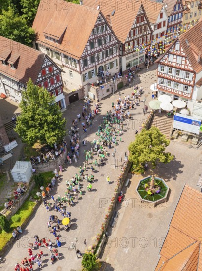Aerial view of a village street with people in parade formation and traditional architecture, 950