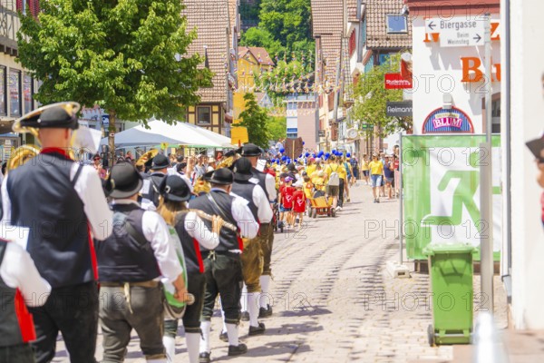 People in traditional costumes march in a sunny village street during a parade, 950 years of Calw,