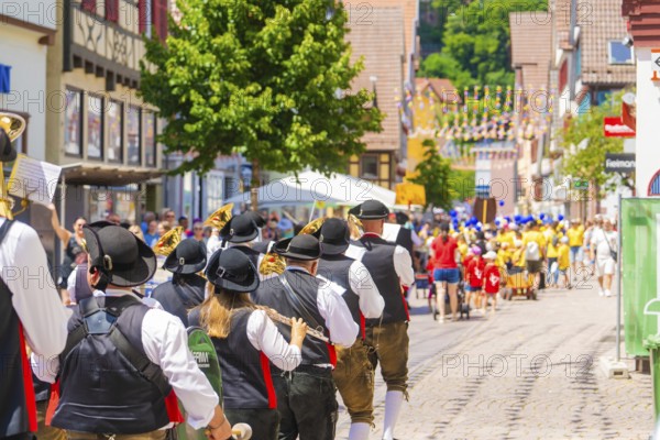 People in traditional costumes musically follow a parade on a sunny village street, 950 years Calw,