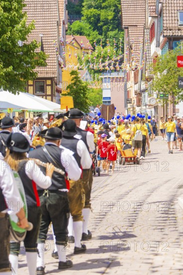 People in traditional dress parade cheerfully through a sunny village street, 950 years of Calw,