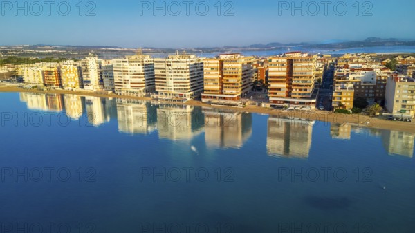 Aerial view of torrevieja skyline reflecting on calm mediterranean sea at sunrise, with colorful