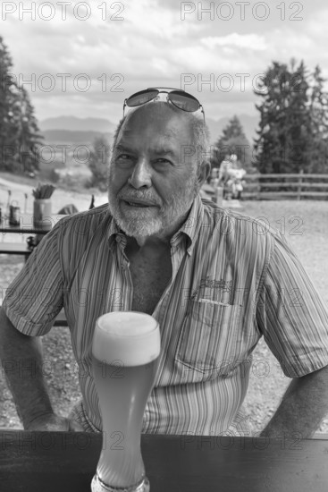 Elderly gentleman with beard and sunglasses in a garden restaurant with a drink, black and white,