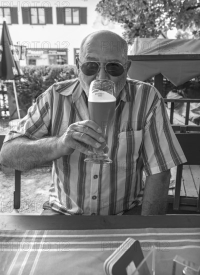 Senior with sunglasses drinking a wheat beer in a beer garden, black and white, Upper Bavaria,