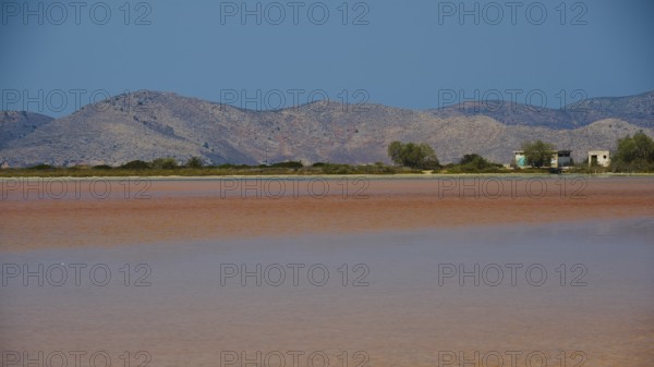 Mountainous landscape with calm lake and small huts under a bright blue sky, salt lake, Tigaki,