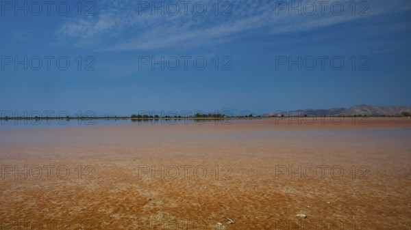 Wide, open landscape with a lake under a narrow blue sky, quiet atmosphere, salt lake, Tigaki,