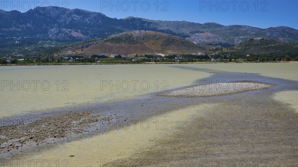 A lake with a long gravel bank and mountains in the background under a blue sky, salt lake, Tigaki,