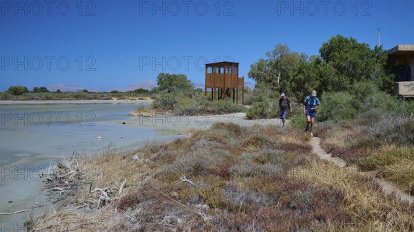 Two hikers on a path next to an observation tower and vegetation, salt lake, Tigaki, nature