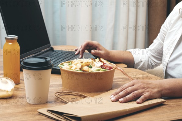 A woman is working on a laptop at home, there is food on the table, salad, coffee and juice,