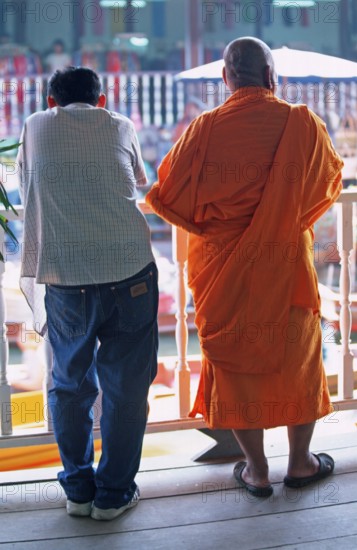 A monk and another man watch the hustle and bustle at Damnoen Saduak Floating Market, Thailand,