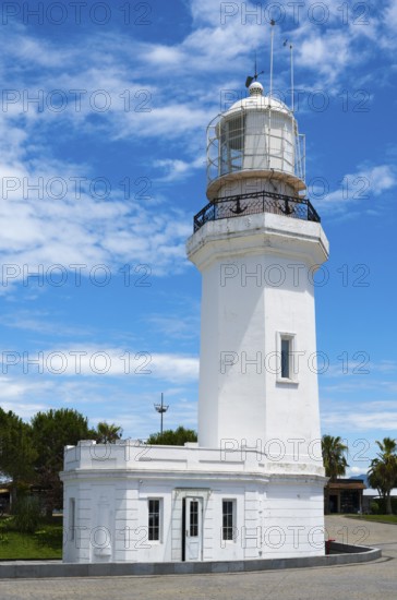 White lighthouse against a blue sky with some clouds and palm trees in the background, lighthouse,