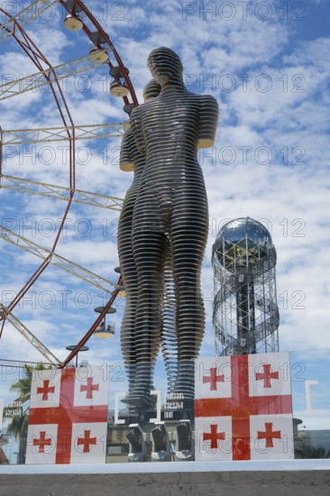 Metal sculptures of a man and a woman in front of a Ferris wheel with Georgian flags, the statue of