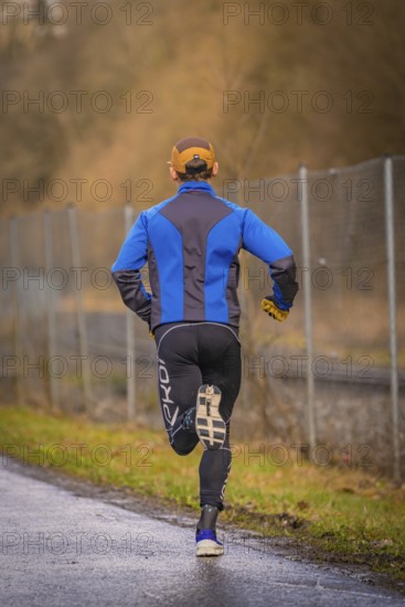 Back view of a runner on a country road wearing blue and black running clothes, triathlon, Calw,