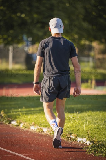A person in sportswear runs on a running track in the middle of a green, summer environment,