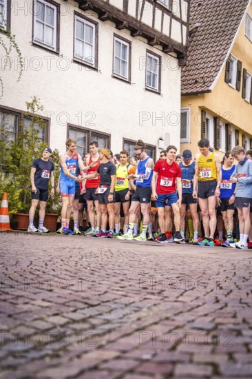 Group of runners at the starting line on a paved road in front of timber-framed houses, triathlon,