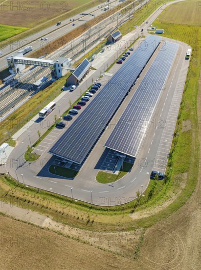 Large parking lot with solar panels along a road and fields, photographed from the air, e-charging