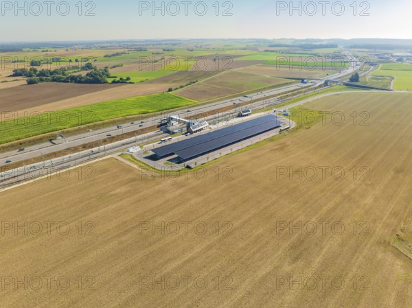 Solar system and motorway run parallel through wide fields under clear skies, e-charging park,