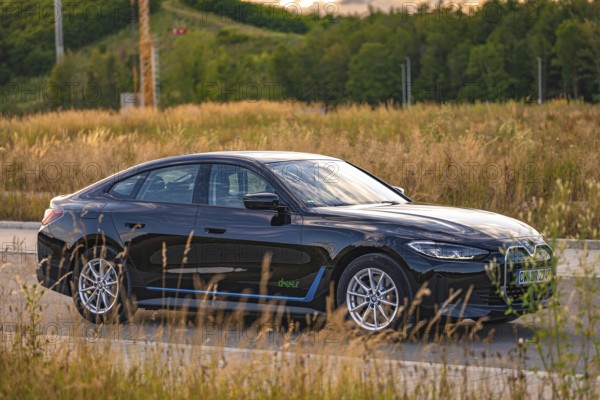 Black car in a field with natural surroundings and road layout, BMW i7 electric car, Deer