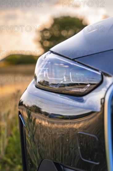 Close-up of a car headlight in the evening, reflecting the surroundings of a field, BMW i7 electric
