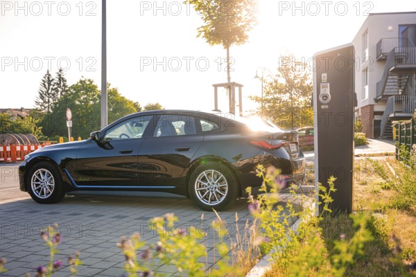 Black BMW at a charging station in an urban environment at sunset, BMW i7 electric car, Deer