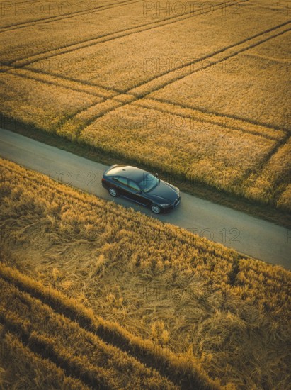A dark car drives on a paved road surrounded by cornfields at dawn or dusk, BMW i7 electric car,