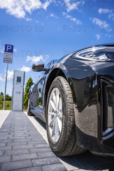 Close-up of a black car next to a parking machine under a blue sky, BMW i7 electric car, Deer