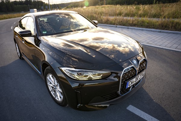 A black car on a road with reflecting sky and a field, BMW i7 electric car, Deer e-Carsharing,