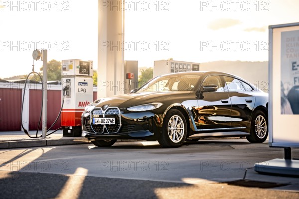Black car at a gas station in the evening sun with modern architecture, BMW i7 electric car, Deer