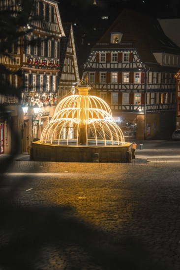 Nocturnal scene with illuminated fountain surrounded by traditional half-timbered houses, Calw,