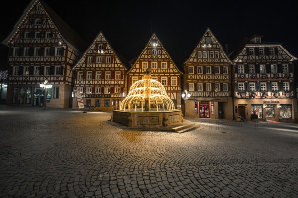 Illuminated fountain in a historic city center with half-timbered buildings at night, Calw, Black