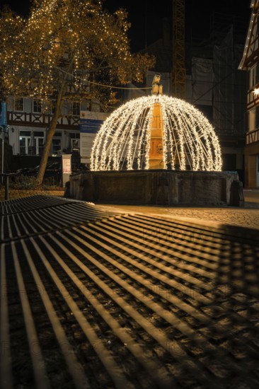 Atmospheric night view of a festive fountain with lights and shadows in an old town, Calw, Black