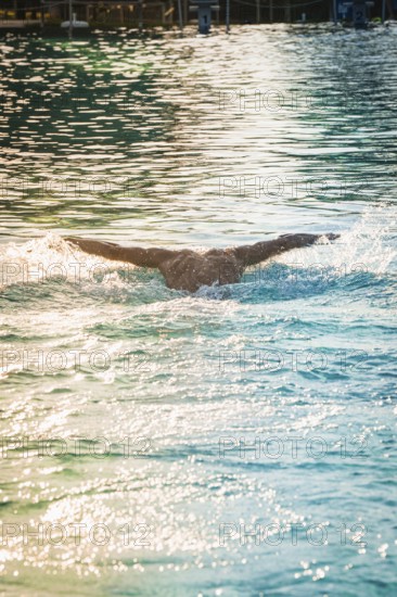 A swimmer in the pool with arms spread out, the water surface shimmers in the light, triathlon,