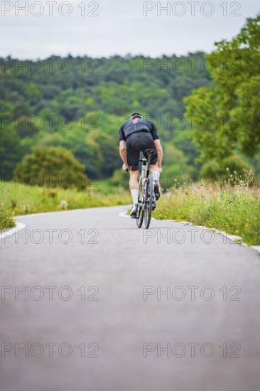 A cyclist rides on a winding road through a wooded area, Triathlon, Calw, Germany