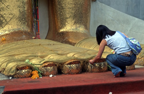 A young woman places flowers on the toes of the standing Buddha at Wat Indrawihan, Bangkok,
