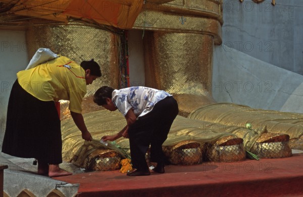Women place flowers on standing Buddha's toes at Wat Indrawihan, Bangkok, Thailand, December 2002,