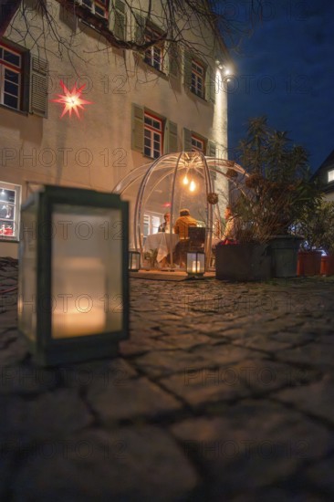 An illuminated dome at night on a stone path flanked by a large candle with windows in the