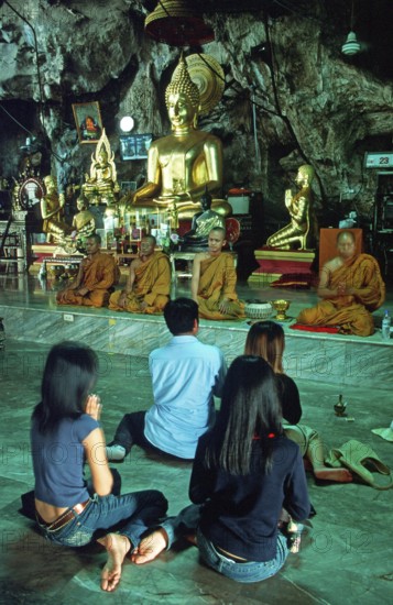 Buddha statue, monks and believers praying, Wat Tam Sua monastery near Krabi, Thailand, December